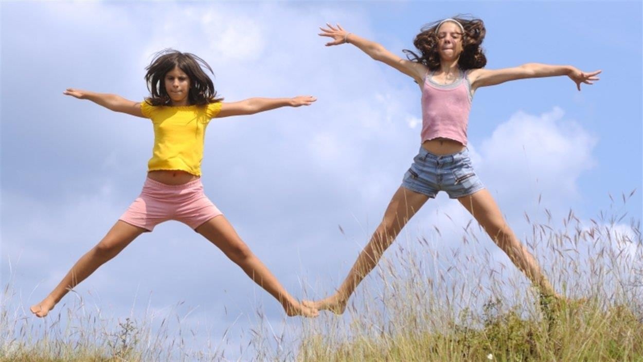 Deux jeunes filles sautent dans un champ d'herbe en faisant des "jumping jack".