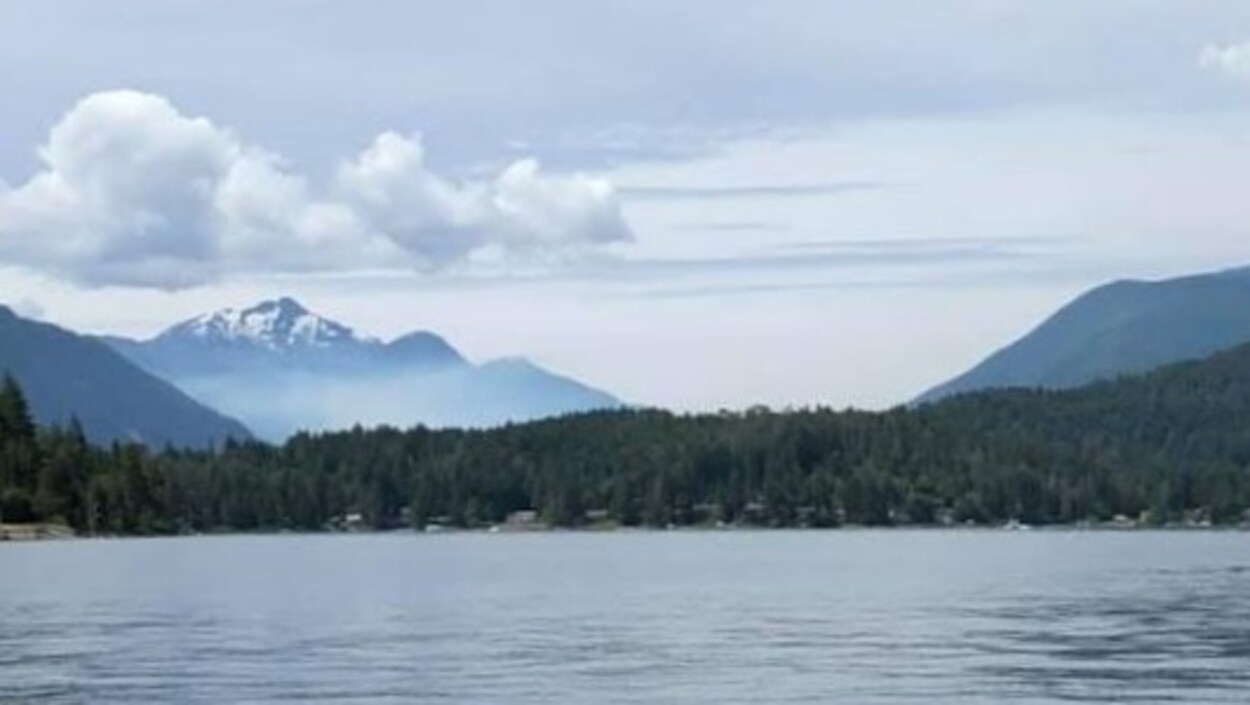 Un lac, une forêt, des montagnes et de la fumée.