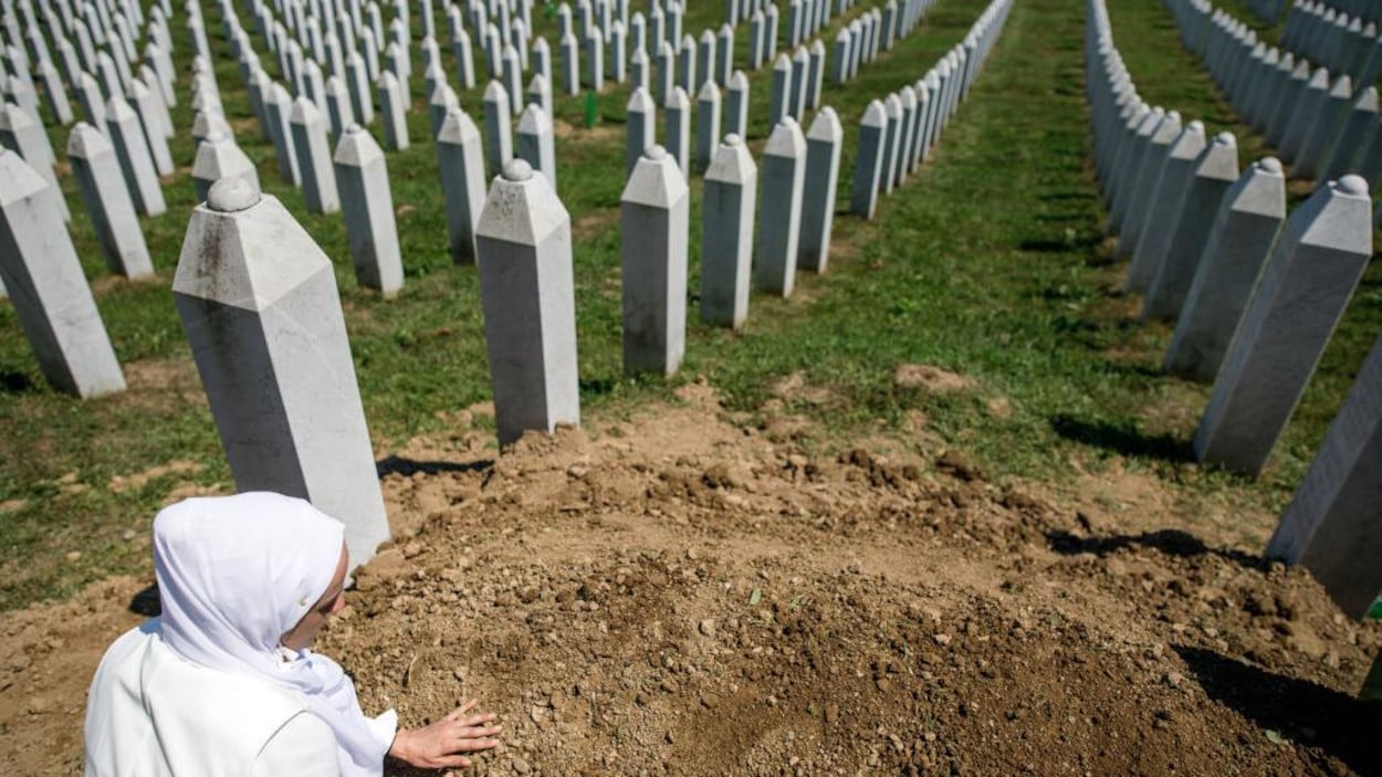 La femme touche la terre devant des milliers de stèles funéraires.