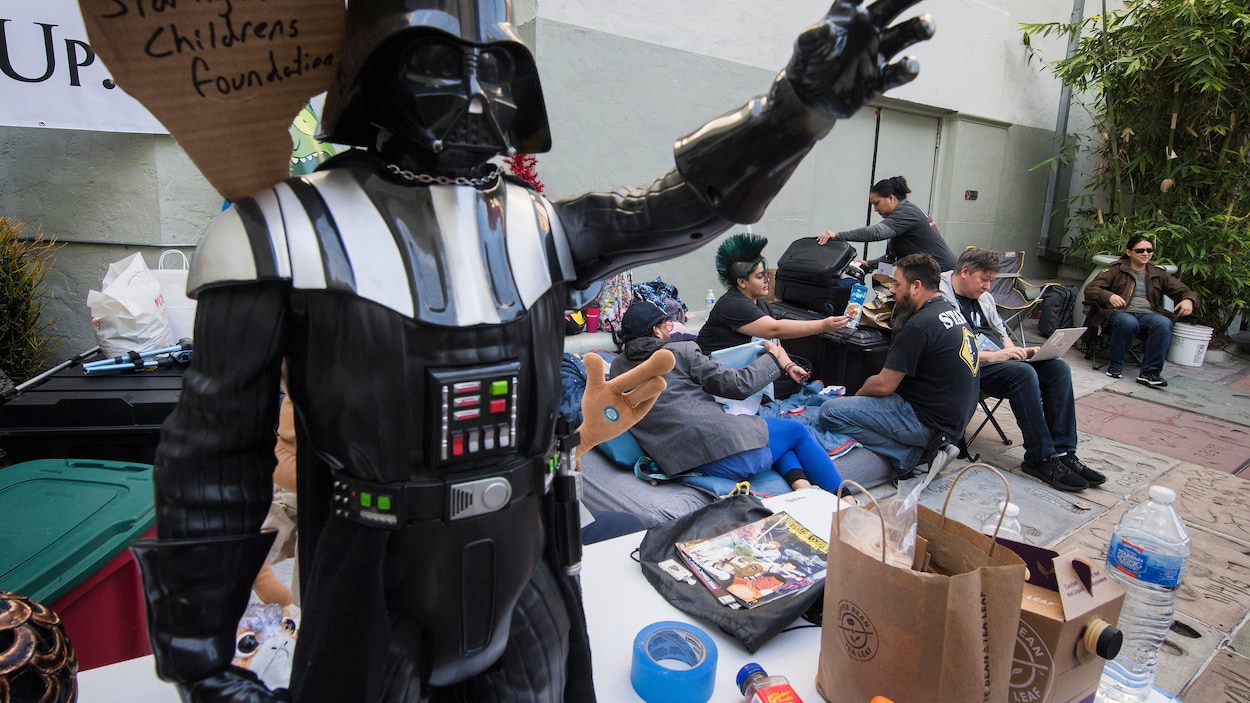 Des personnes sont assises sur des chaises de camp. Une figurine de Dark Vader trône sur une table.