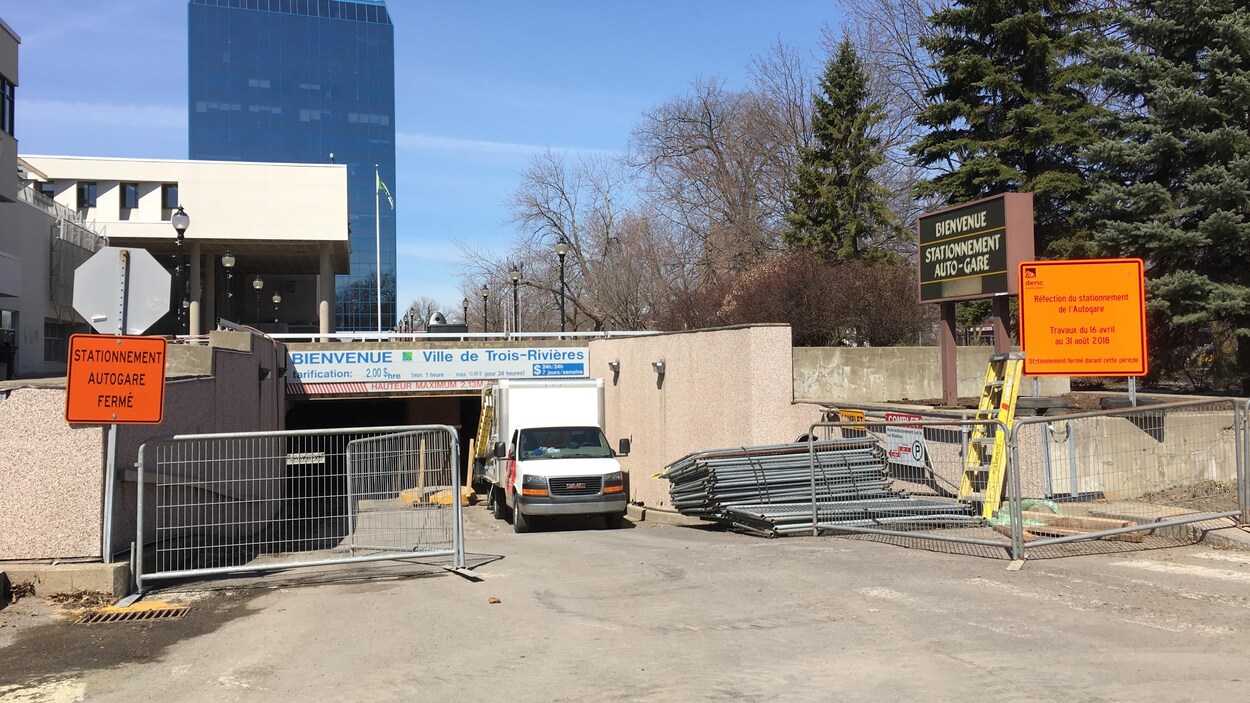 À l'entrée du stationnement souterrain, des clôtures, un camion et des pancartes orange indiquant la fermeture du stationnement.
