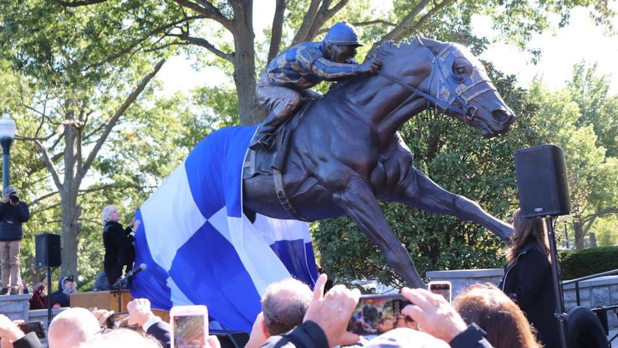 Une femme retire le drapeau bleu et blanc pour dévoiler le monument du cheval monté par un jockey.