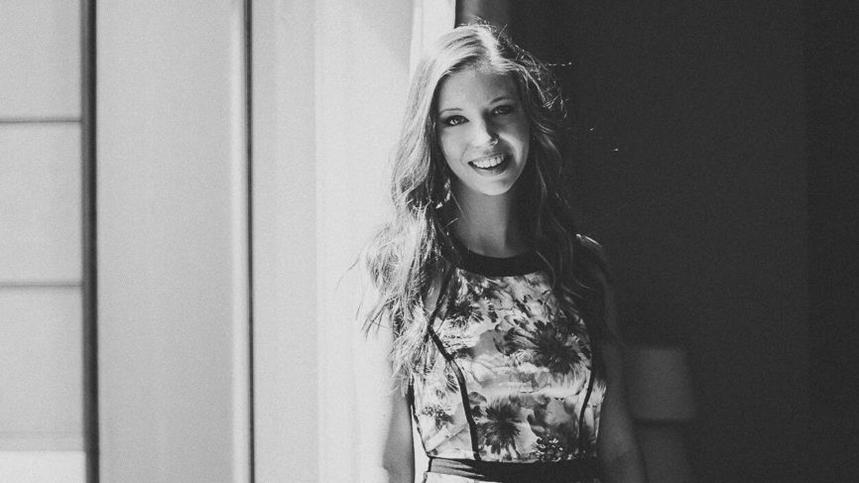 Portrait en noir et blanc, en extérieur, de l'autrice Stellerine Huez, devant un cadre de porte. Elle porte une robe fleurie et les cheveux lâchés.