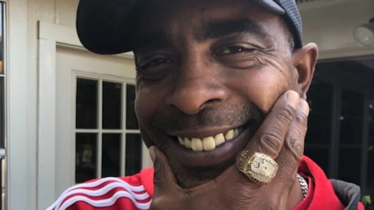 Un homme noir sourit avec une grosse bague sur sa main tient son visage.