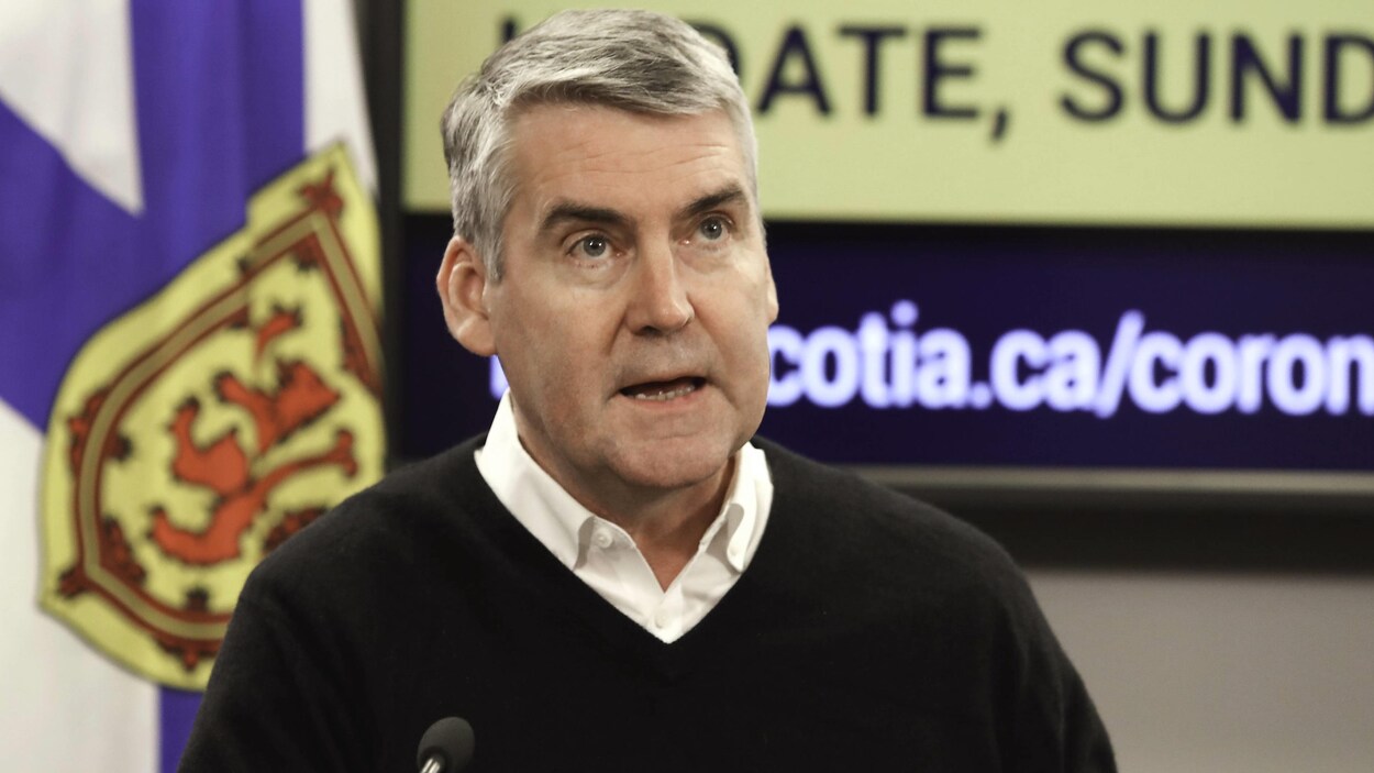 Stephen McNeil devant un drapeau de la Nouvelle-Écosse et un écran de télévision.