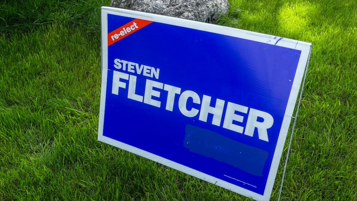 Une affiche plantée dans une pelouse où est écrit en anglais Élisez à nouveau Steven Fletcher. Dans le bas à droite un logo du Parti conservateur a été caché à la peinture bleu, mais on peut encore le voir un peu.