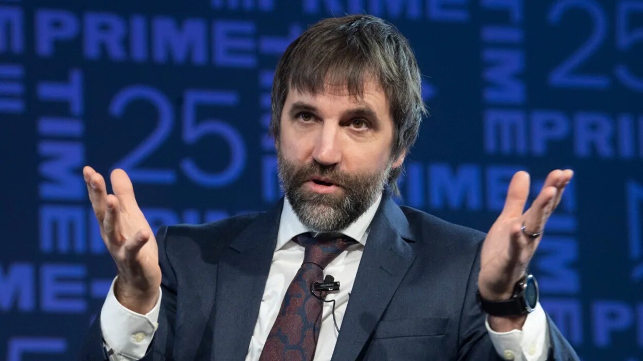 Le ministre prend la parole. Il est assis et porte un micro-cravate.