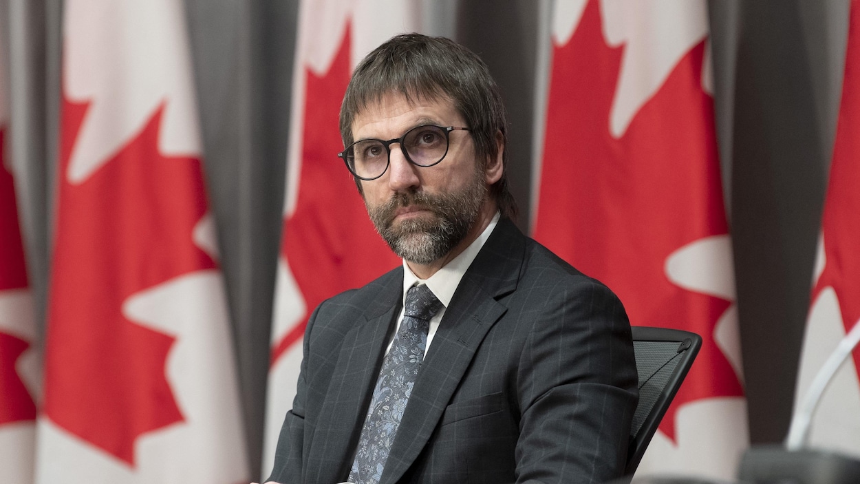 Steven Guilbault devant une rangée de drapeaux canadiens.