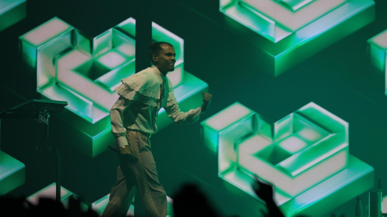 Stromae sur scène devant un fond d'écran vert. 