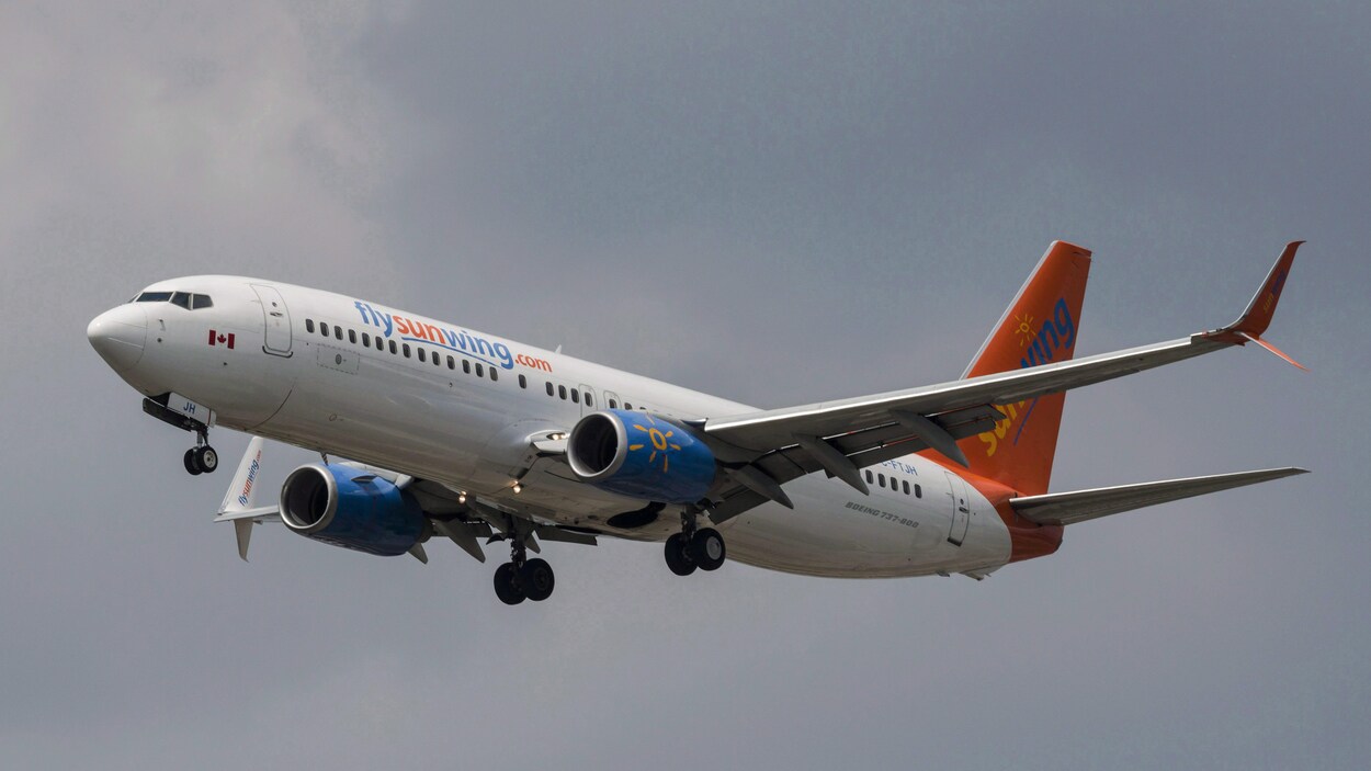 Un avion de Sunwing aux couleurs orange et bleue dans le ciel.