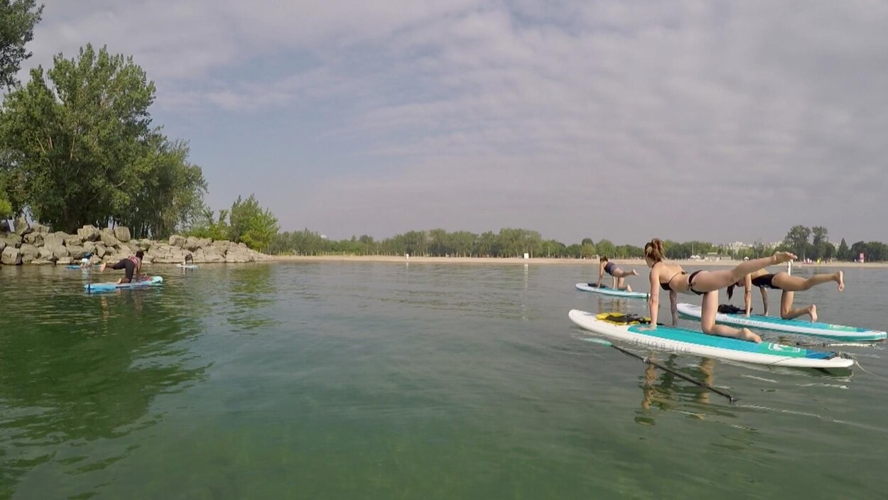 Des participants font une pose de yoga sur une planche à pagaie sur un lac.