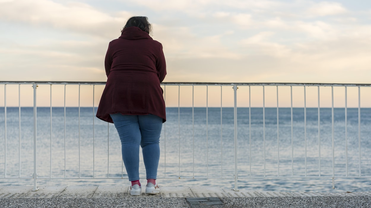 Une femme regarde la mer qui s'étend devant elle.