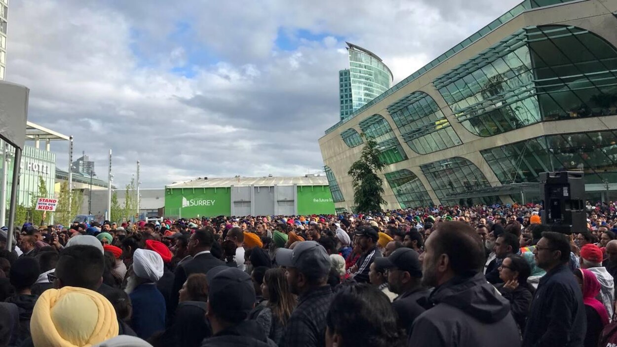 Des milliers de personnes sont entassées sur une grande place devant un immeuble de quelques étages. Des milliers de personnes sont entassées sur une grande place devant un immeuble de quelques étages.