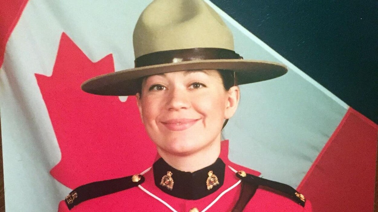 Plan serré d'une policière de la Gendarmerie royale du Canada habillée de l'uniforme de parade rouge avec un drapeau du Canada en arrière-plan.