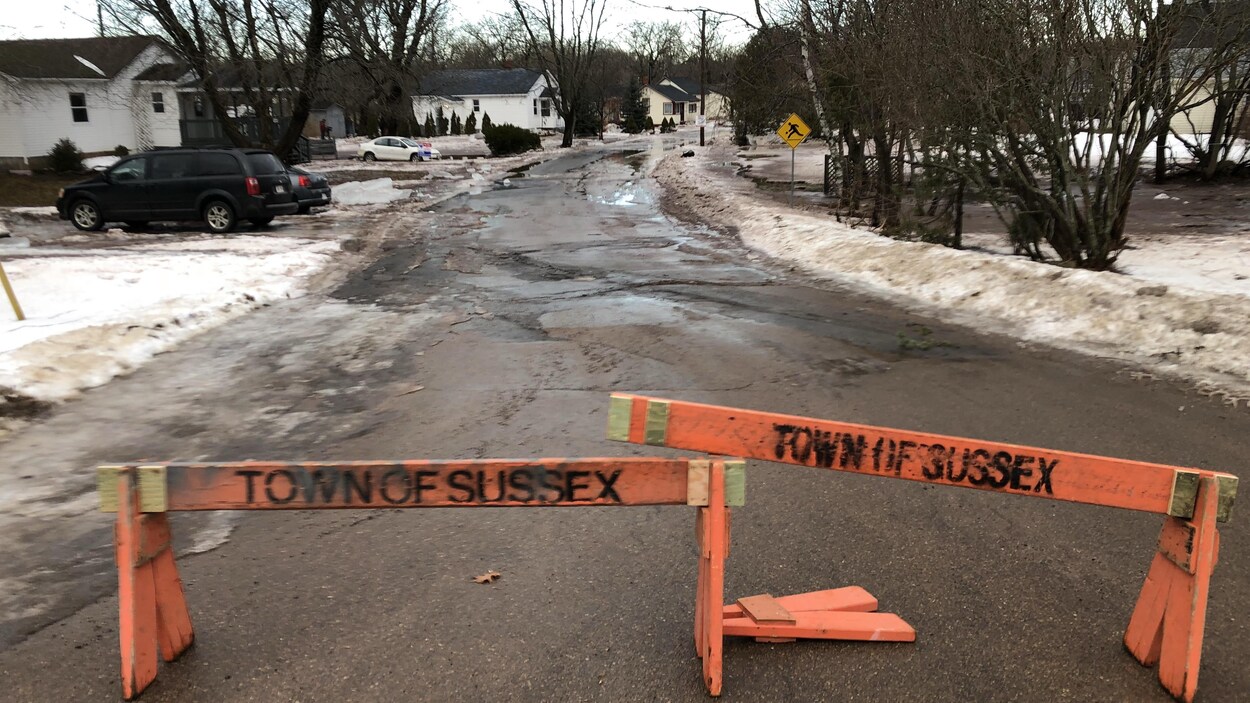 Des barrières des travaux publics bloquent le passage dans la rue partiellement inondée.