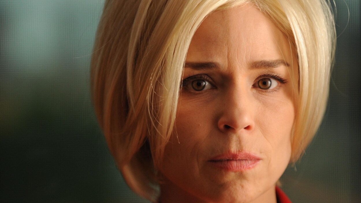 L'actrice porte une perruque blonde et regarde la caméra.