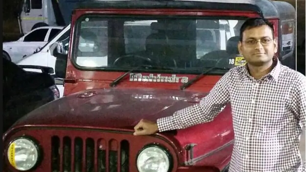 Kalpesh Patel pose à côté d'une voiture rouge.
