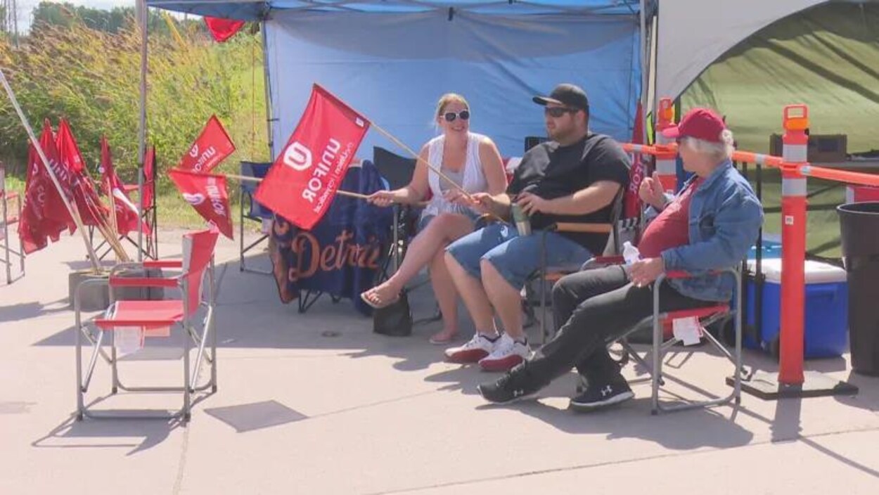 des membres d'Unifor font la grève, ils sont assis et ont des pancartes unifor