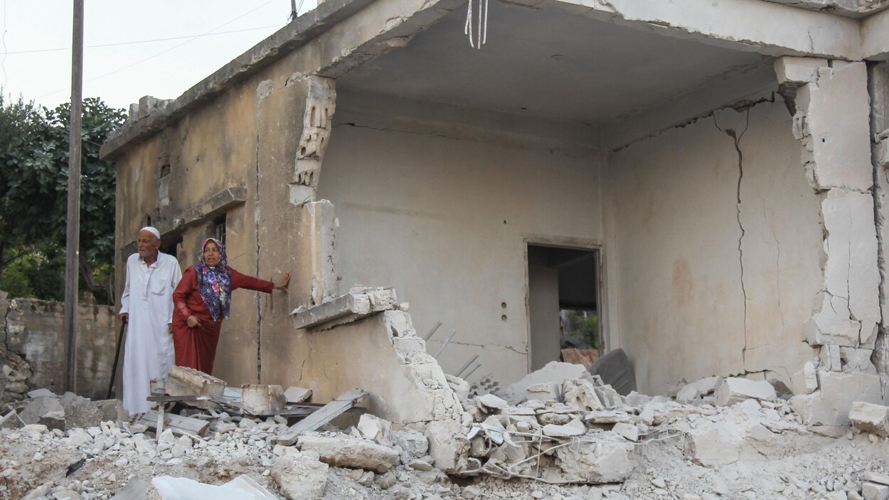 Un couple regarde les décombres d'une maison bombardée.