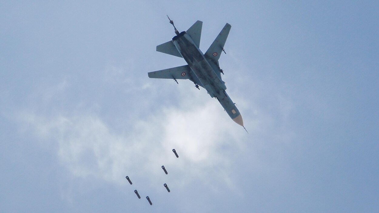 Un avion militaire laissant tomber 6 petites bombes, vu d'en-dessous.