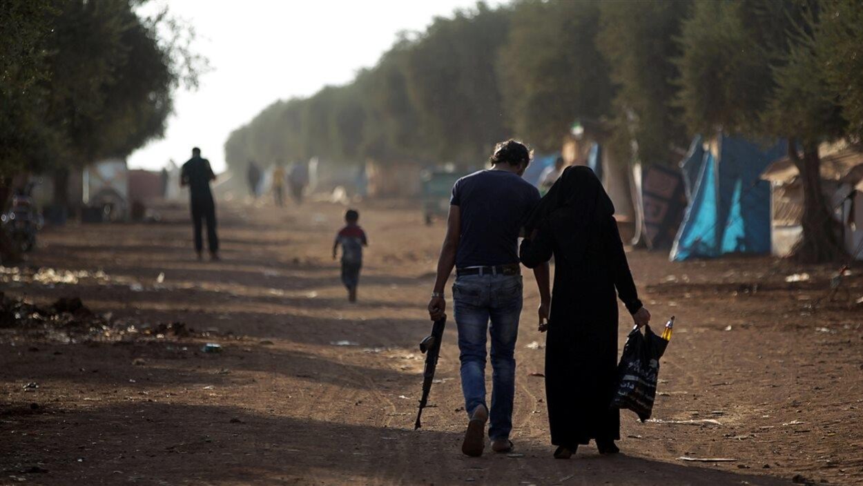 Un homme armé se déplace aux côté d'une femme dans un camp de réfugiés dans le nord d'Alep. Un homme armé se déplace aux côté d'une femme dans un camp de réfugiés dans le nord d'Alep.