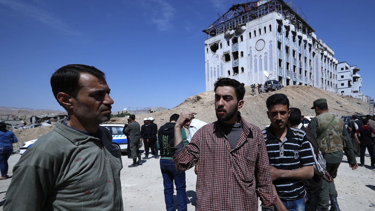 Plusieurs hommes sont rassemblés devant un hôpital de Douma, visiblement endommagé par des obus. Des militaires syriens sont situés tout près. Plusieurs hommes sont rassemblés devant un hôpital de Douma, visiblement endommagé par des obus. Des militaires syriens sont situés tout près.