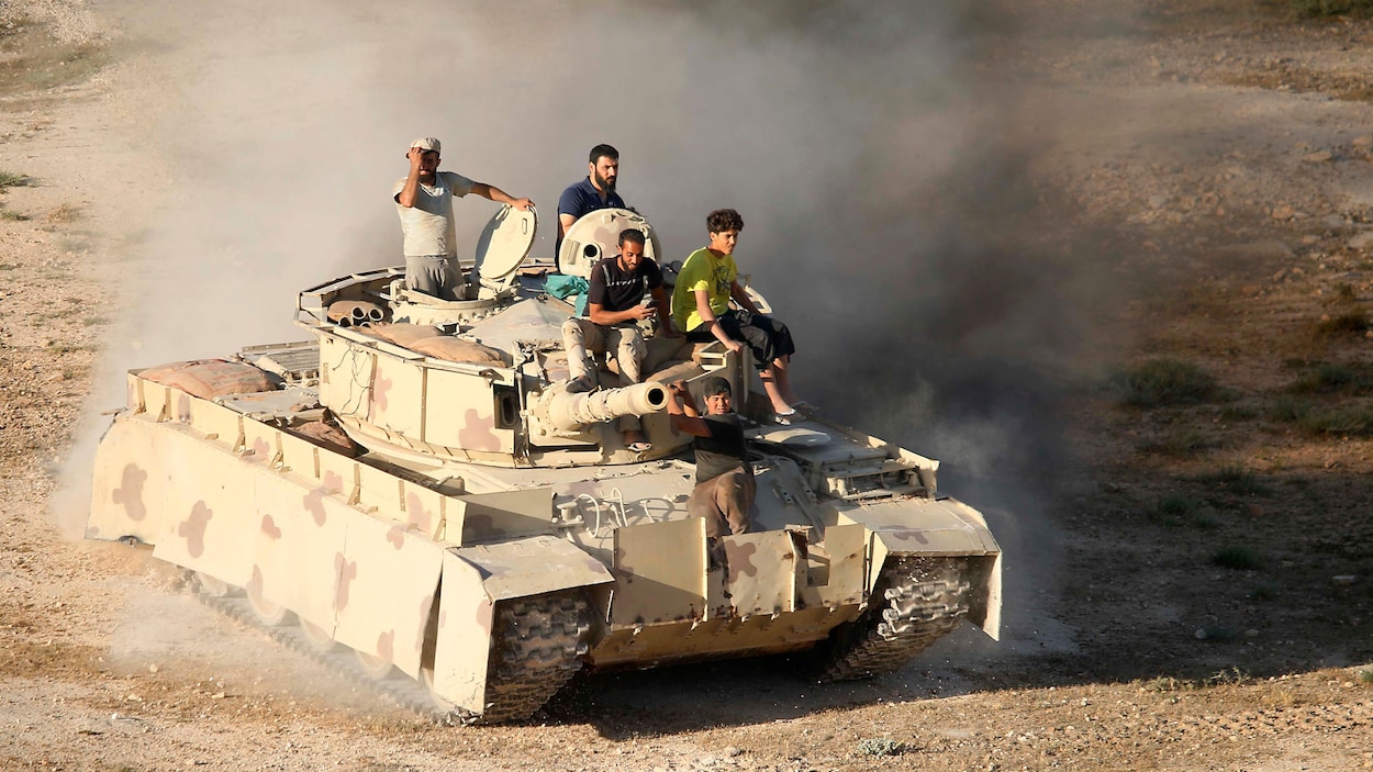Cinq rebelles syriens sont sur un char d'assaut roulant sur une route et soulevant de la poussière. Cinq rebelles syriens sont sur un char d'assaut roulant sur une route et soulevant de la poussière.