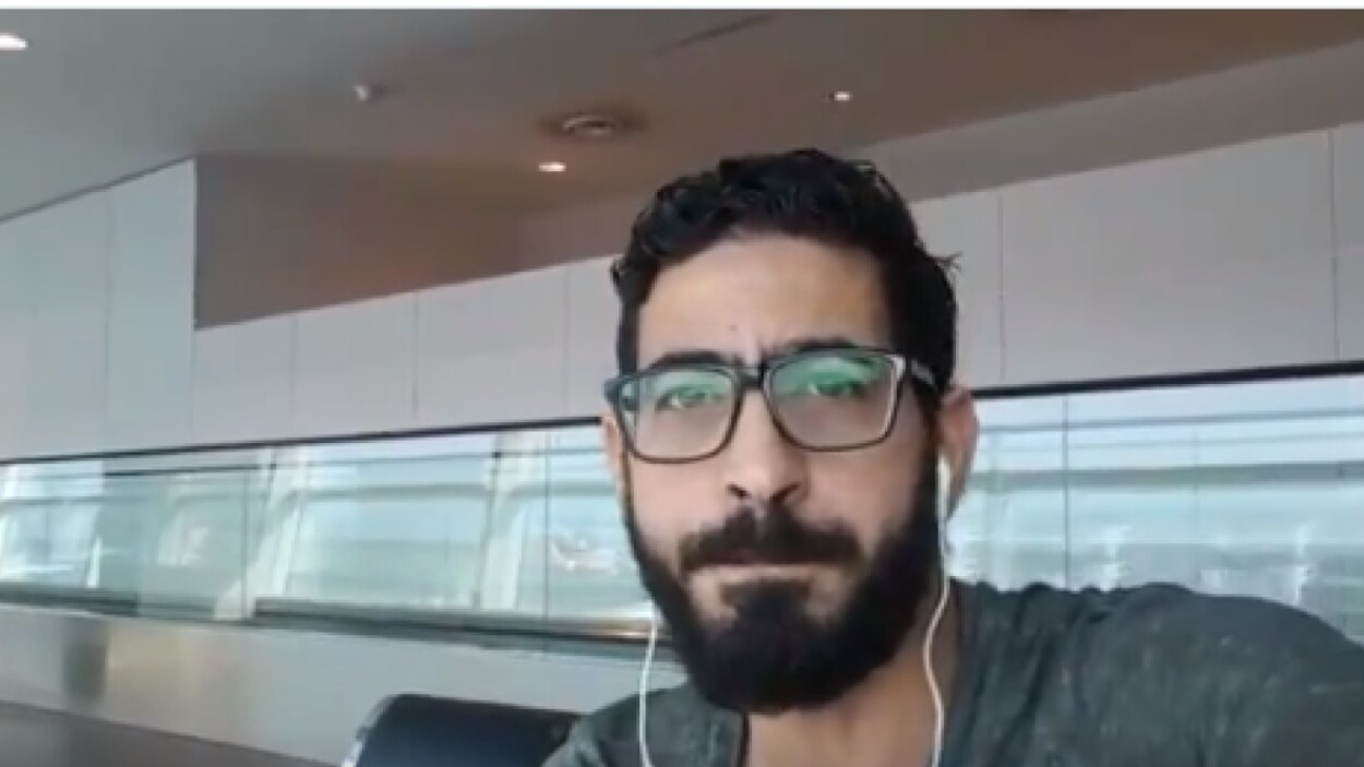 Gros plan sur le visage d'un jeune homme barbu et portant des lunettes de vue, qui regarde la caméra dans un égoportrait.