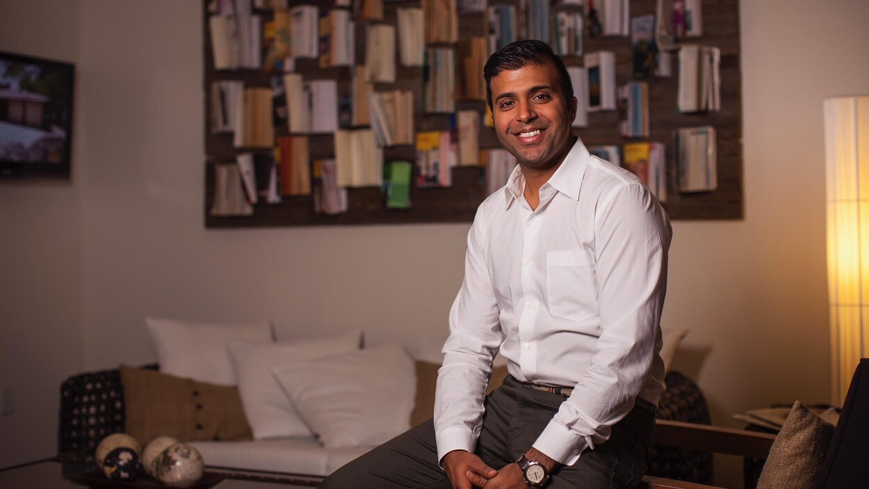 Un homme souriant pose dans un appartement.