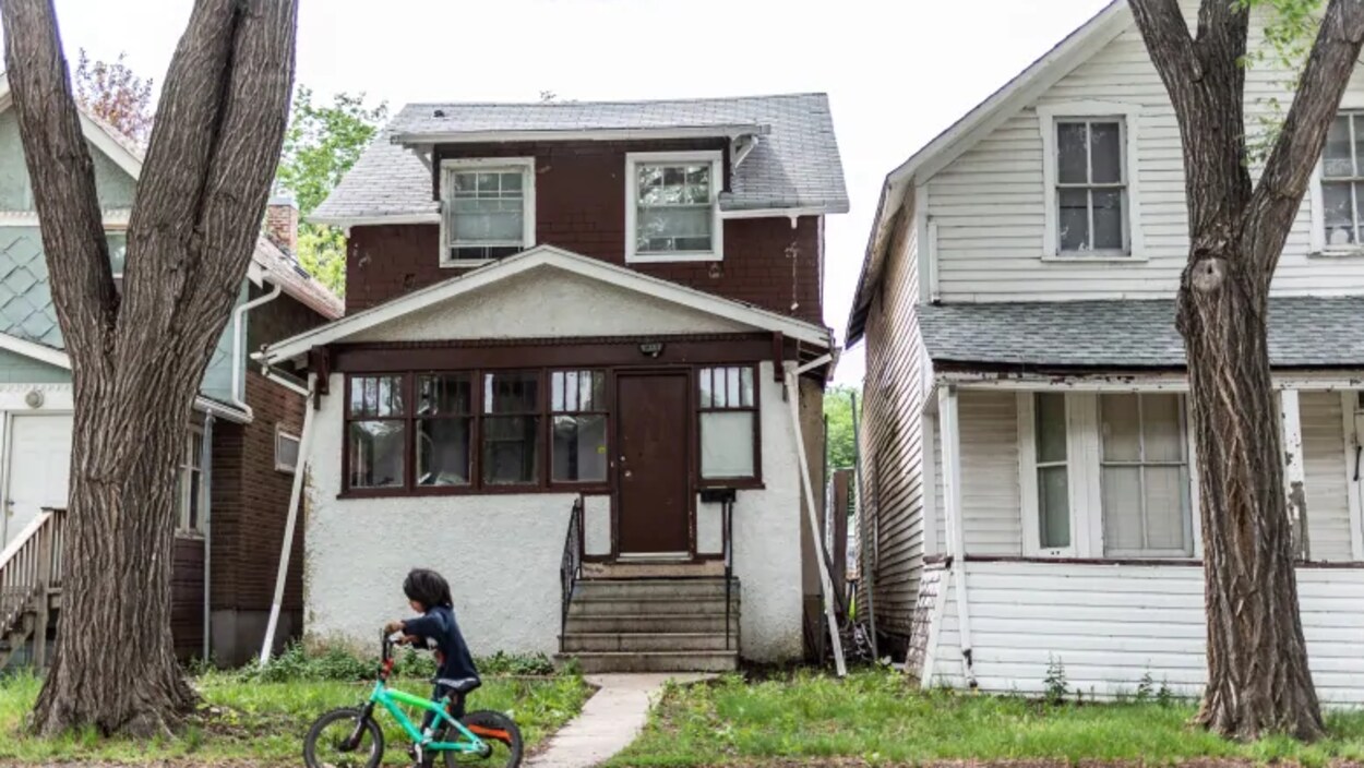 Un petit garçon passe en vélo devant une maison blanche et brune.