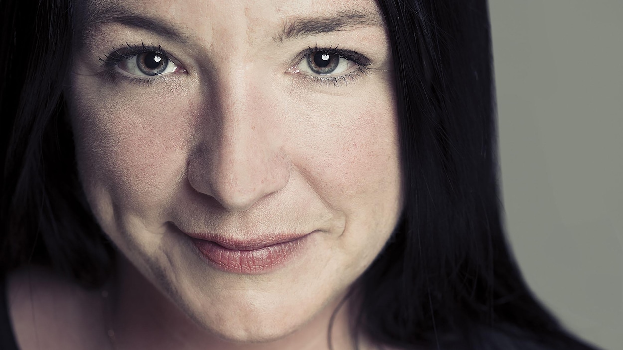 Portrait en couleur de la poète Tania Langlais, en légère plongée. Elle porte un haut noir sans manches, des cheveux noirs longs et une chaîne avec un pendentif de perles autour du cou.