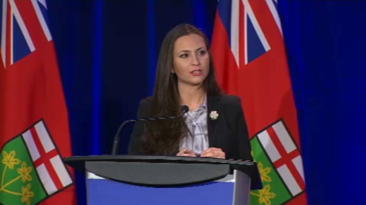 Tanya Granic Allen derrière un lutrin et un microphone.