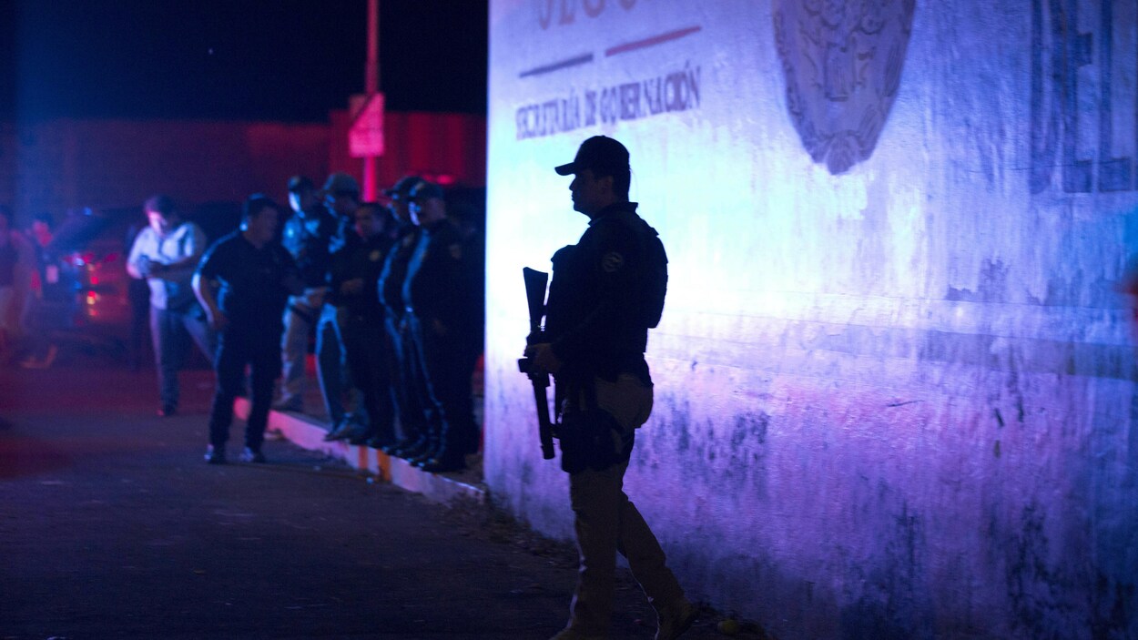 Un policier fédéral se tient à l'extérieur du centre de rétention des migrants. Il fait nuit.