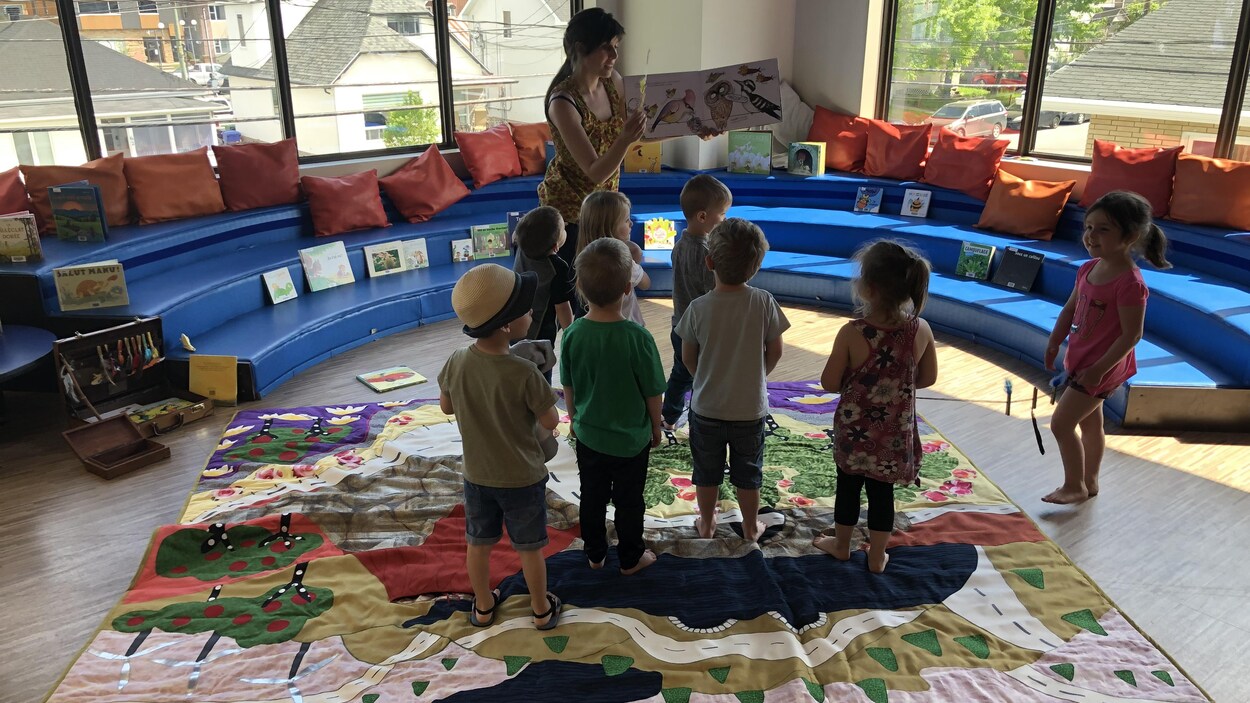 Des enfants écoutent une femme leur faire la lecture sur un tapis d'éveil.