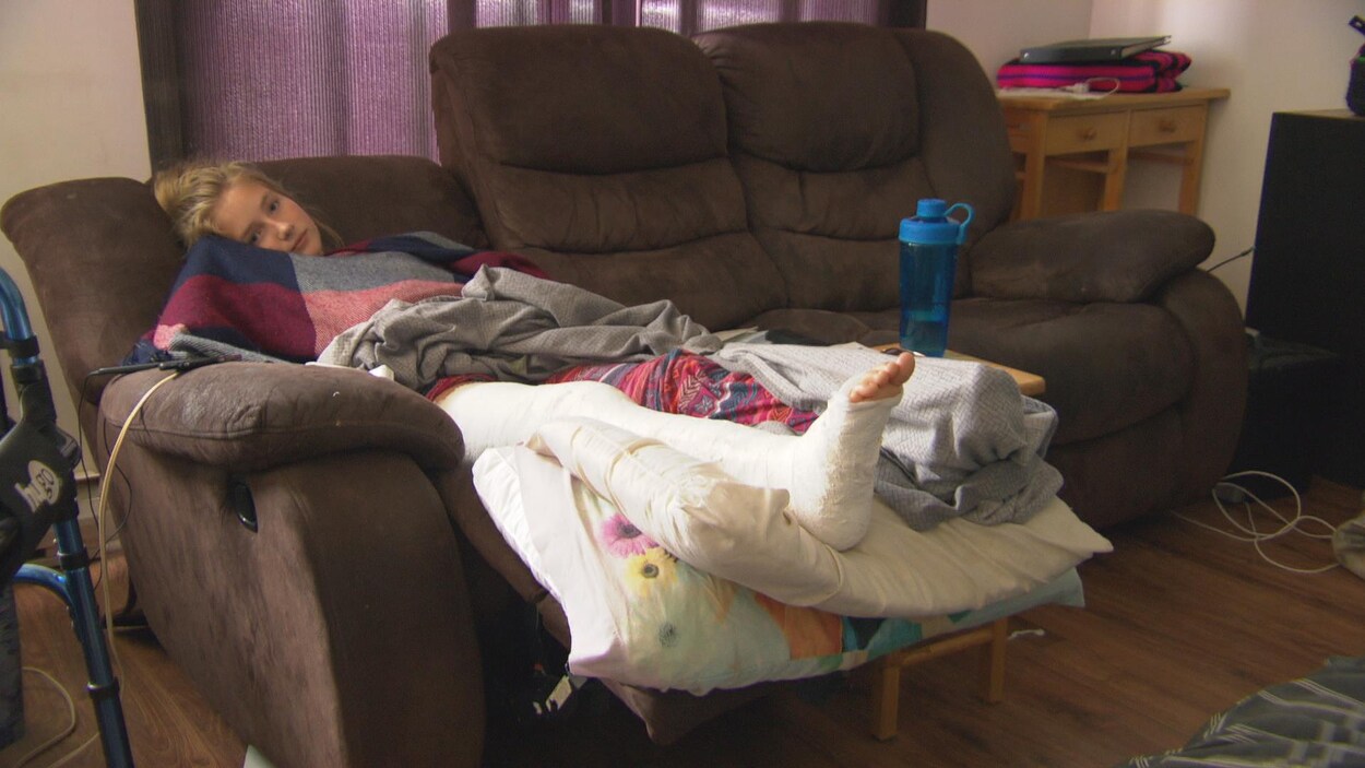 Une adolescente avec la jambe recouvert d'un plâtre est couchée sur un divan.
