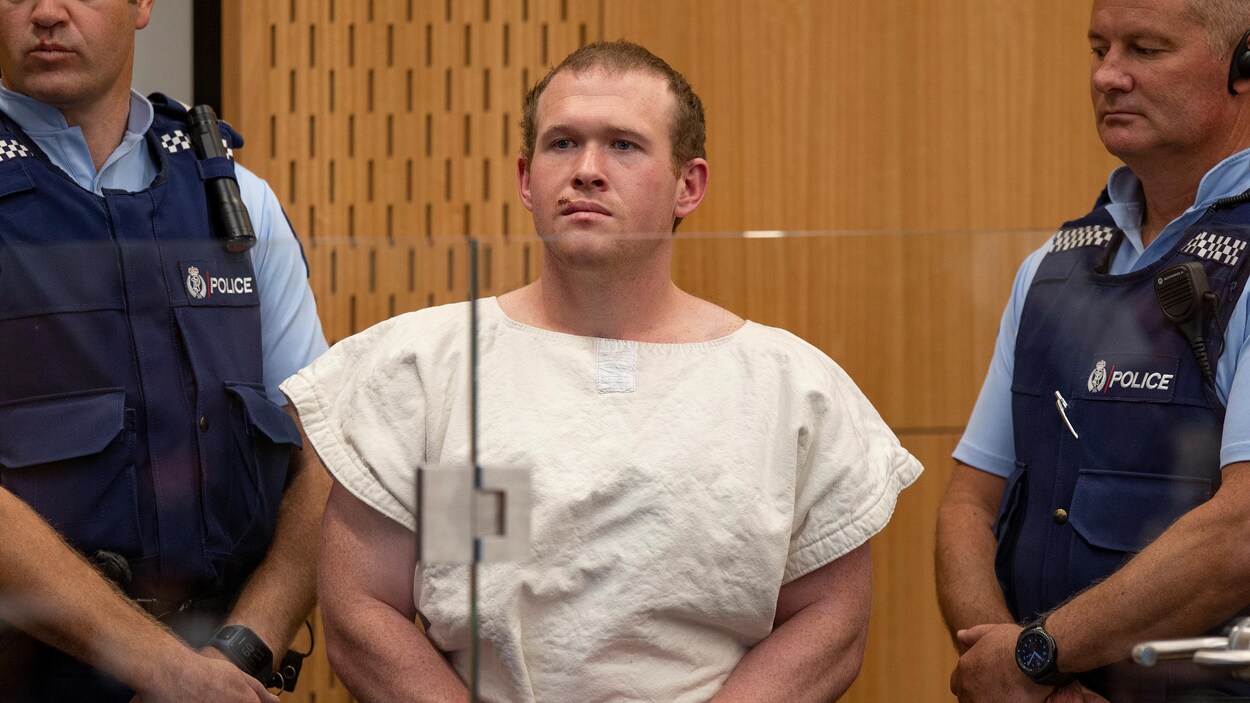 Tarrant, dans un tribunal, entre deux policiers.