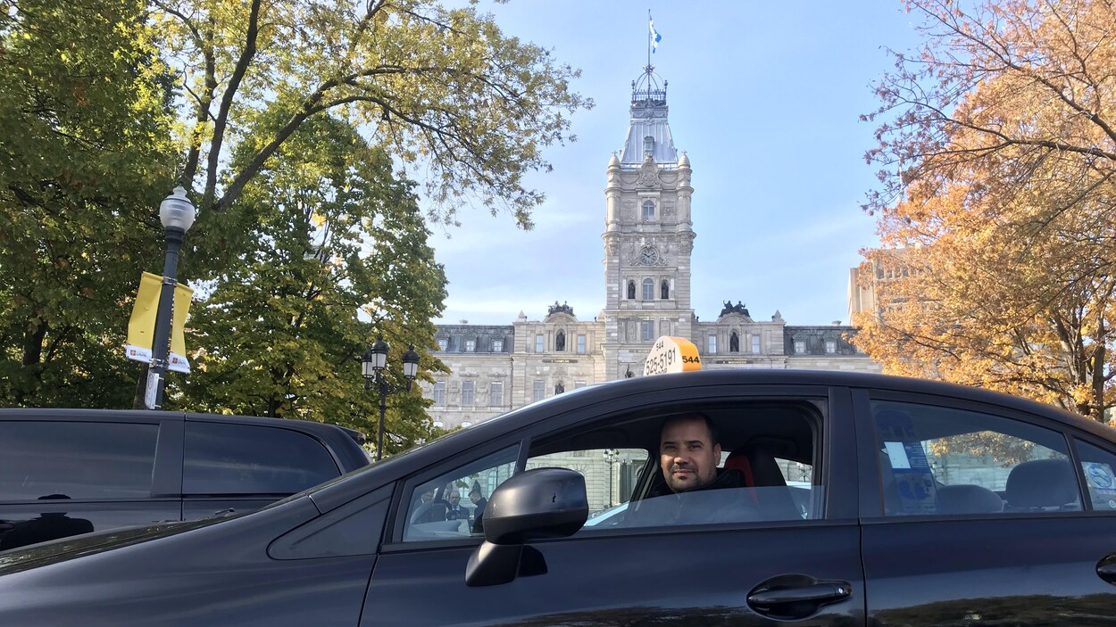 Un chauffeur de taxi dans son véhicule noir devant l'Assemblée nationale