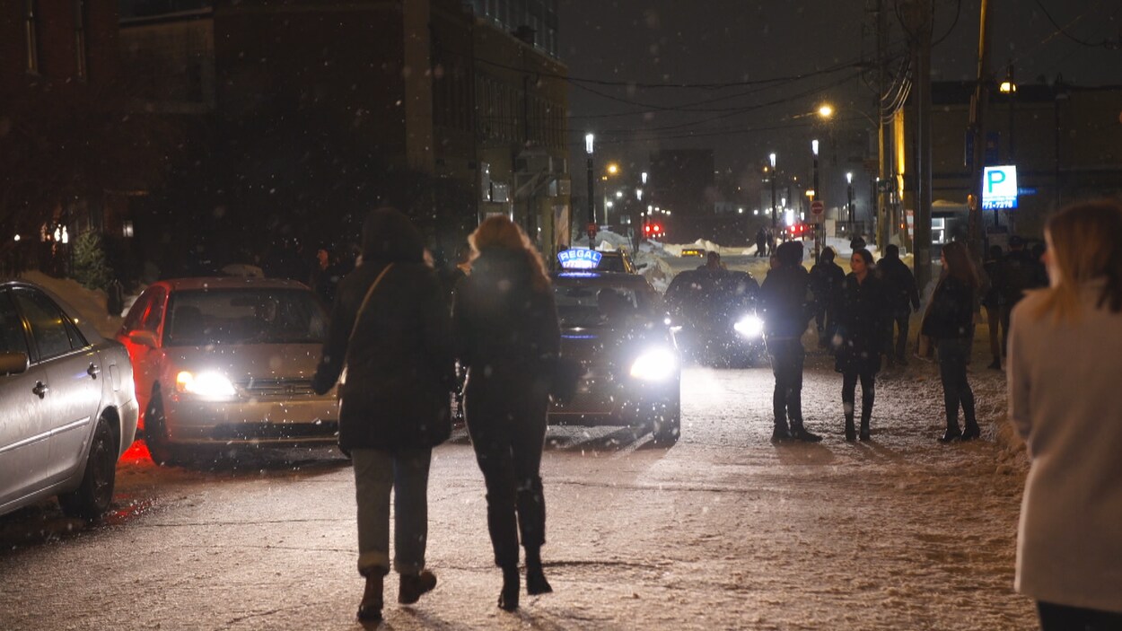Des personnes marchent dans la rue et sur les trottoirs du Vieux-Hull la nuit, l'hiver, alors que des voitures tentent de circuler.
