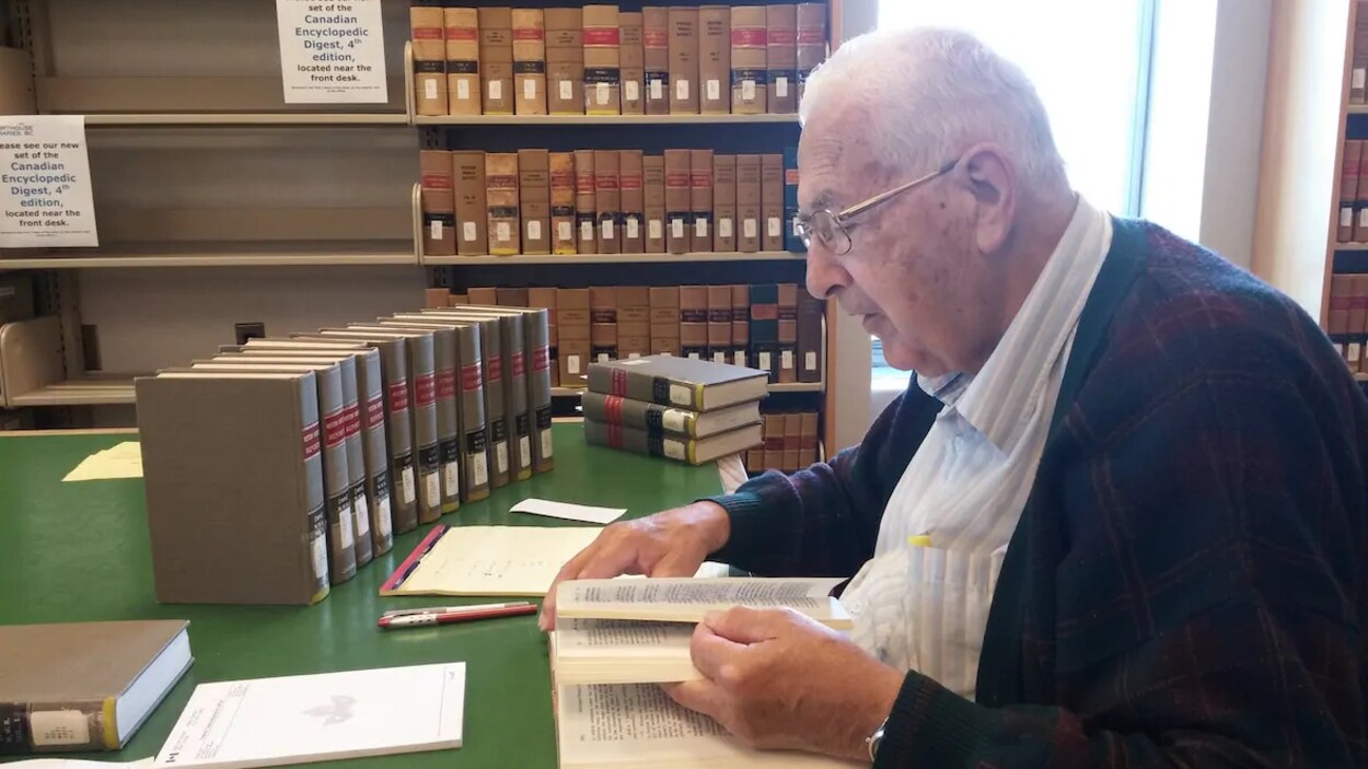 Ted Hughes assis à une table en train de feuilleter un livre dans la bibliothèque du palais de justice de Victoria.