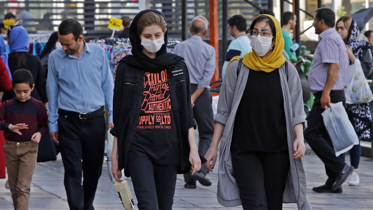 Des femmes et des hommes, dont certains portent des masques de protection, circulent dans une de la capitale iranienne.