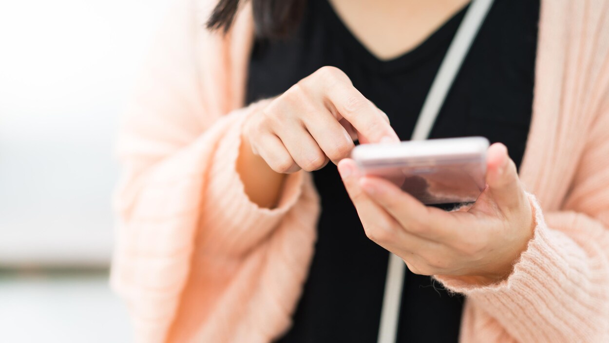 Une jeune femme appuie sur l'écran de son téléphone cellulaire.