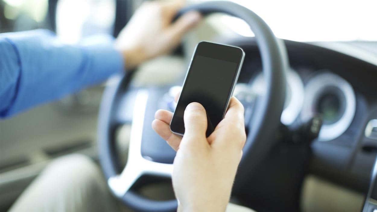 Un conducteur tient un téléphone cellulaire au volant de sa voiture.
