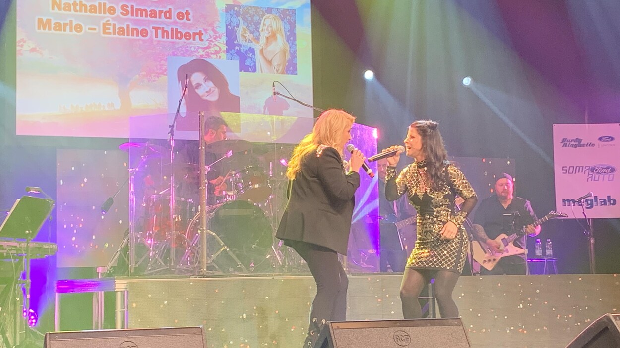 Deux femmes chantent sur une scène. Des musiciens jouent derrière elles.