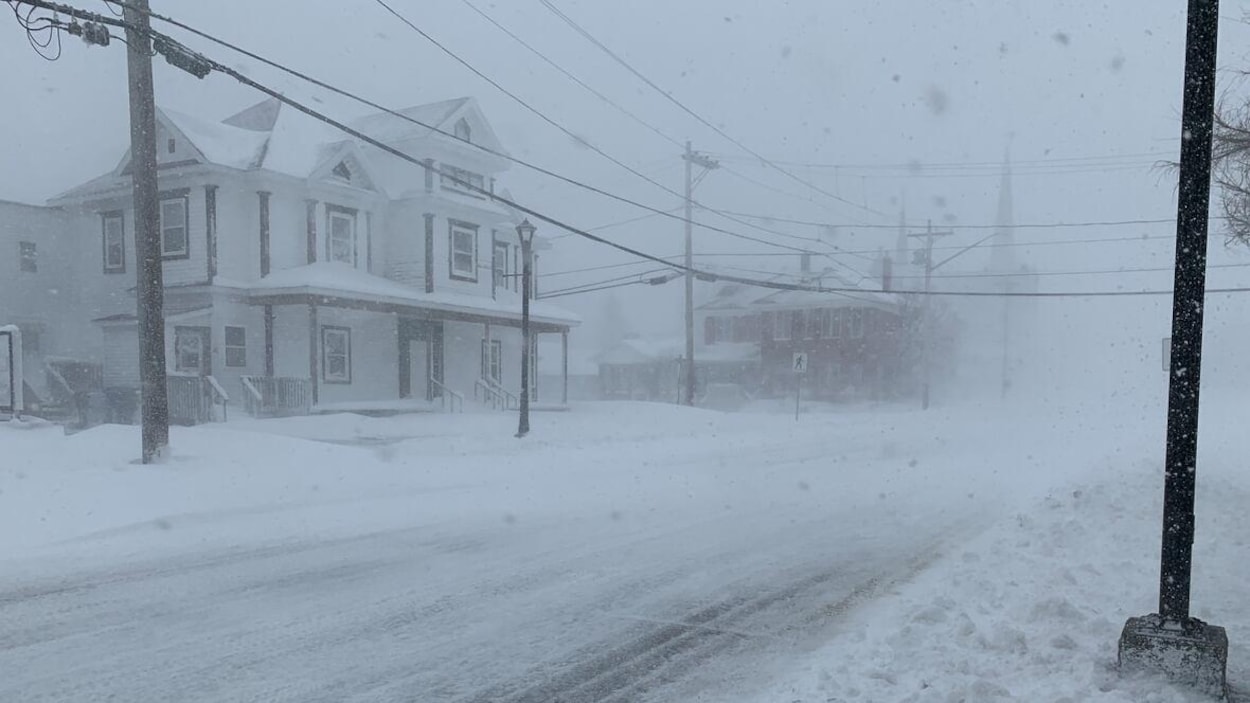 La neige tombe sur une rue déjà enneigée pendant une tempête.