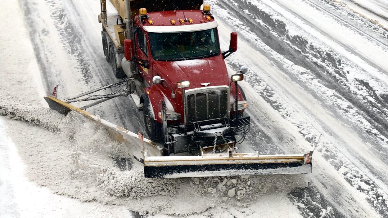 Une déneigeuse pousse de la neige sur une rue enneigée.