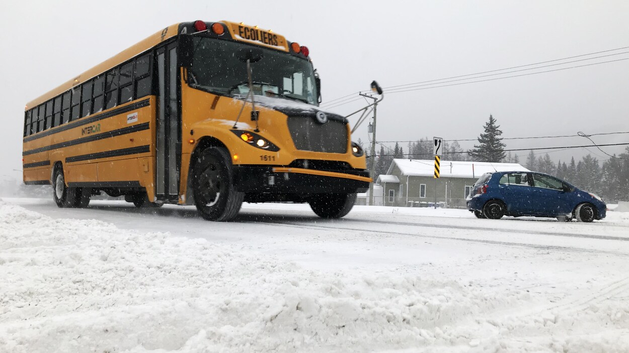 Un autobus scolaire circulant sur une route enneigée.
