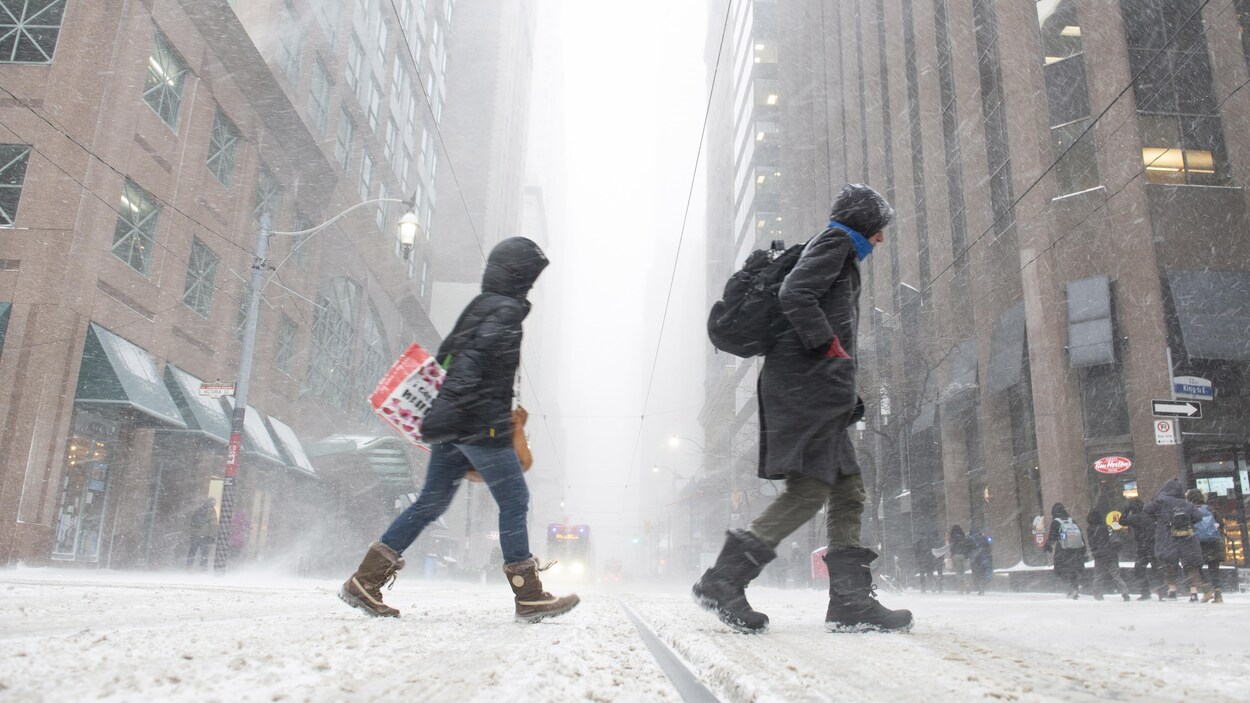 Des piétons traversent une rue du centre-ville de Toronto pendant une tempête de neige.