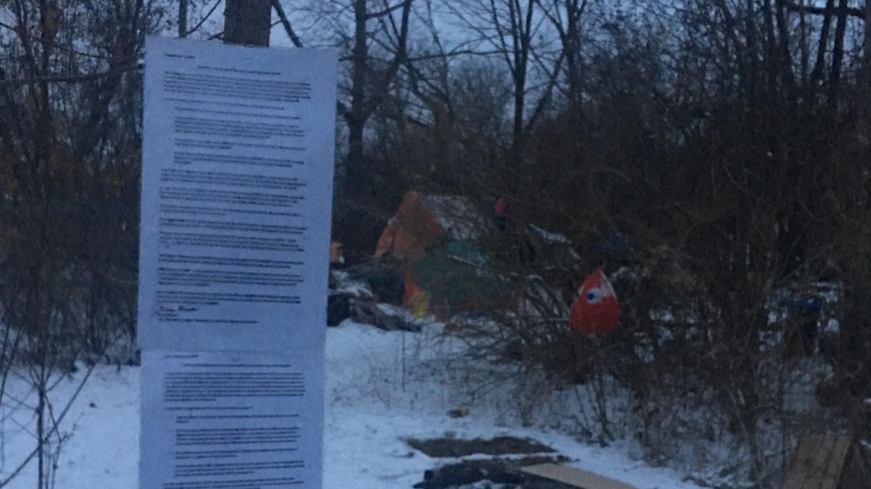 Des feuilles de papier agrafées sur un arbre près d'une tente autour de laquelle sont éparpillés des déchets.