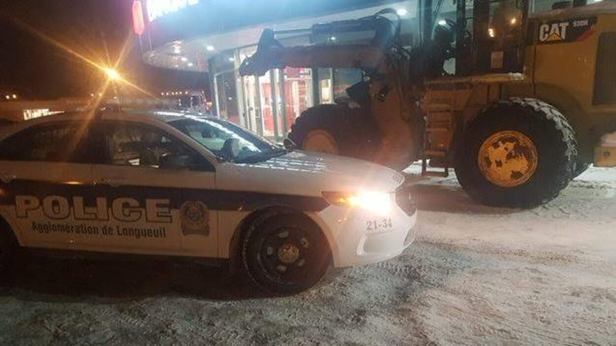 Une voiture du Service de police de l'agglomération de Longueuil devant une excavatrice