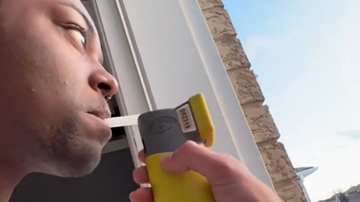 Un homme souffle dans un éthylotest tenu par un policier, à la porte de sa maison.
